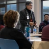 Person standing talks to a group sitting at a rectangular table.