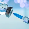 Closeup photo of a needle being injected into a syringe with blue background.