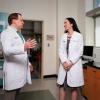Two researchers in white coats talk in their lab.
