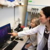 A person in a lab coat points to a computer screen as a student looks at the screen.