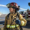 A female firefighters looks into the distance wearing full firefighting gear.