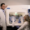 Noel Warfel and doctoral candidate Caitlyn Flores work in the lab in front of cell culture workstation with sleeves.