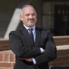 An outdoor portrait of John Ruiz with arms crossed wearing a suit and tie.