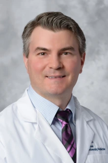 Artyom Abramyan in a white lab coat and pink and black plaid tie with light blue checked shirt.