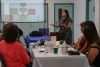 A woman with long brown hair speaks to people sitting at a table.