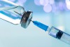 Closeup photo of a needle being injected into a syringe with blue background.