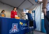 Two students assist at the Skin Cancer event booth. A young boy plays a giant Jenga on the table while his father looks on and take a photo.