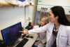 A person in a lab coat points to a computer screen as a student looks at the screen.